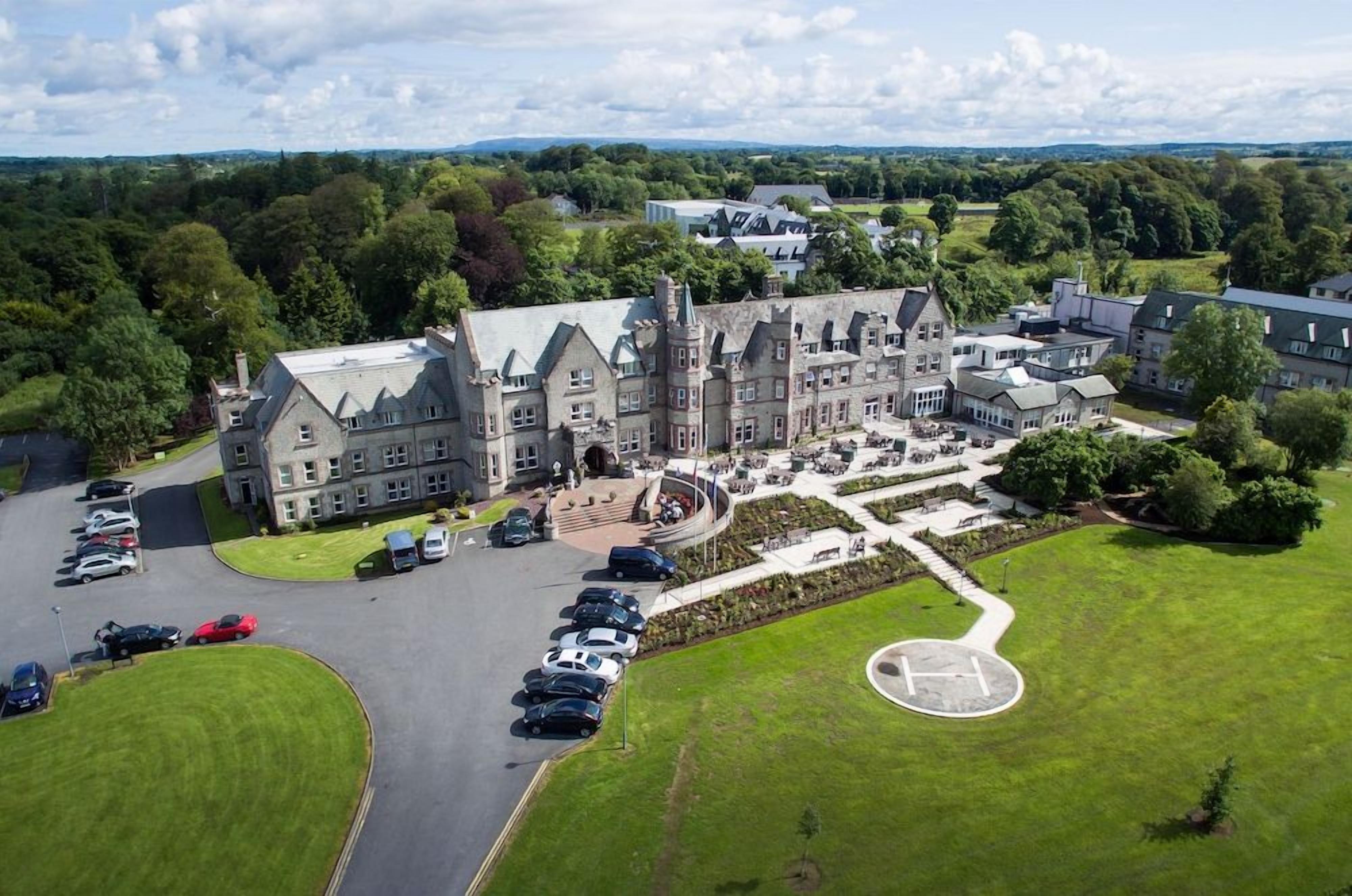 A large, historic building with multiple wings, a central courtyard, and a parking area.