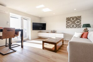 Ein modernes Wohnzimmer mit Flachbildfernseher, einer Couch, einem Couchtisch und einem Essbereich mit Stuhl und Tisch.