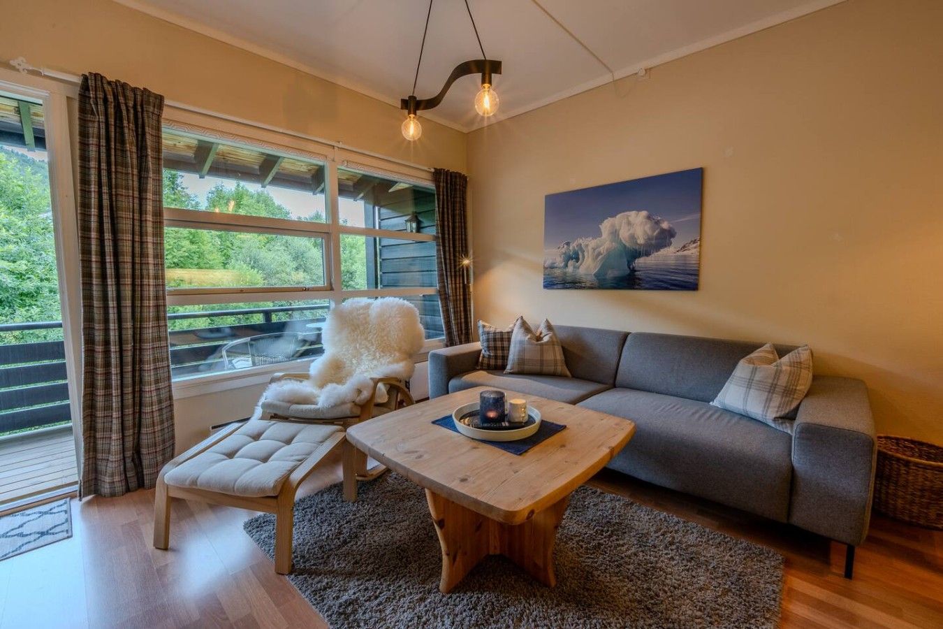Un salon chaleureux avec un canapé, un fauteuil, une table basse et une vue sur l’extérieur grâce à de grandes fenêtres.