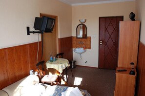 A small, simple room with a bed, a table with chairs, a sink, a mirror, a television mounted on the wall, and a wardrobe. - Bona (Kraków)