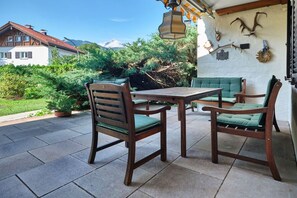 Eine Terrasse im Freien mit einem Holztisch und -stühlen, umgeben von viel Grün und Blick auf die Berge.
