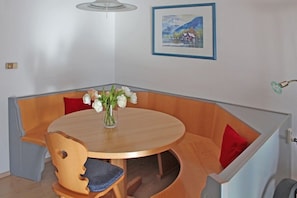 A corner dining area with a round table, wooden chairs, a vase of flowers, and a framed picture on the wall. - Holiday home "Kanzelwand" (Lechbruck)