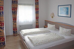 Ein Hotelzimmer mit zwei Betten, einem Heizkörper, einem Nachttisch, einer Lampe und einem gerahmten Bild an der Wand.