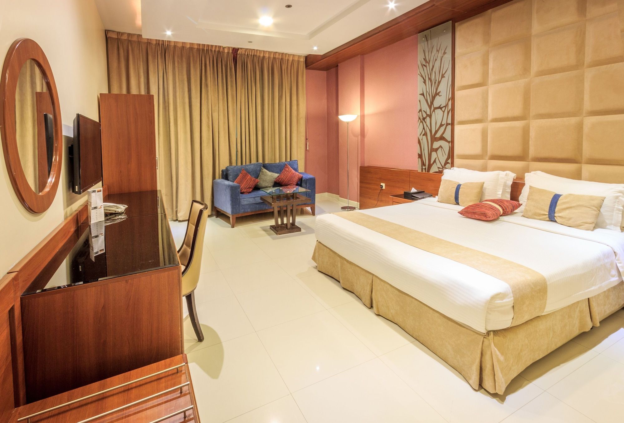 A hotel room with a large bed, a desk with a chair, a sofa, and a large mirror.