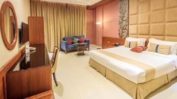 A hotel room with a large bed, a desk with a chair, a sofa, and a large mirror.