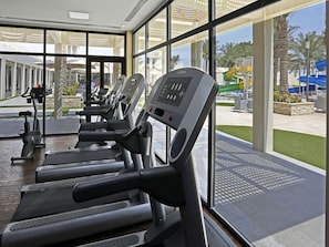 A gym with treadmills and exercise equipment, large windows, and a view of a water park. - Dana Beach Resort AL Khobar (Abqaiq)