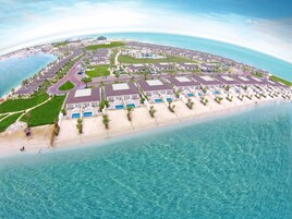 Vista aérea de un complejo turístico costero con varios edificios hoteleros, piscinas y una playa.