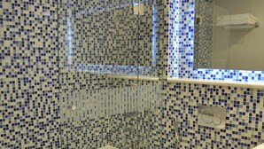 Ett badrum med väggar beklädda med mosaik, en dusch med glasväggar, en toalett och ett handfat.