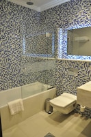 Casa de banho com paredes em mosaico, cabine de duche envidraçada, sanita e lavatório.