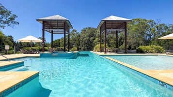 Una piscina con agua azul cristalina, rodeada de sillones de playa y sombrillas, y dos gazebos de madera.