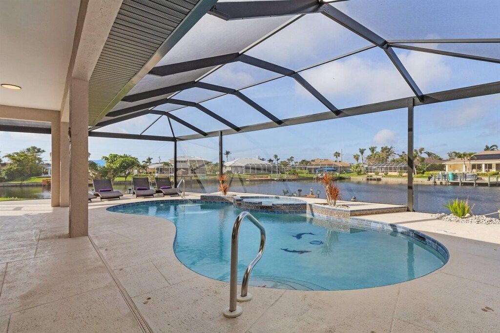A covered outdoor swimming pool with lounge chairs and a view of a body of water and buildings in the background.