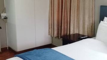 Une chambre d’hôtel avec un lit, une armoire et un rideau.