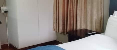 A hotel room with a bed, a wardrobe, and a curtain.