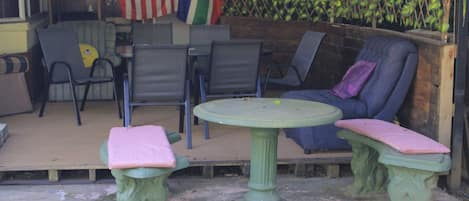 An outdoor seating area with two green tables and chairs, a bench, and an American flag.