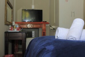 A hotel room with a bed, a television on a wooden stand, and a small table with a cup and a bottle. - Room-alexandra Bed and Breakfast Room 1 (Pietermaritzburg)