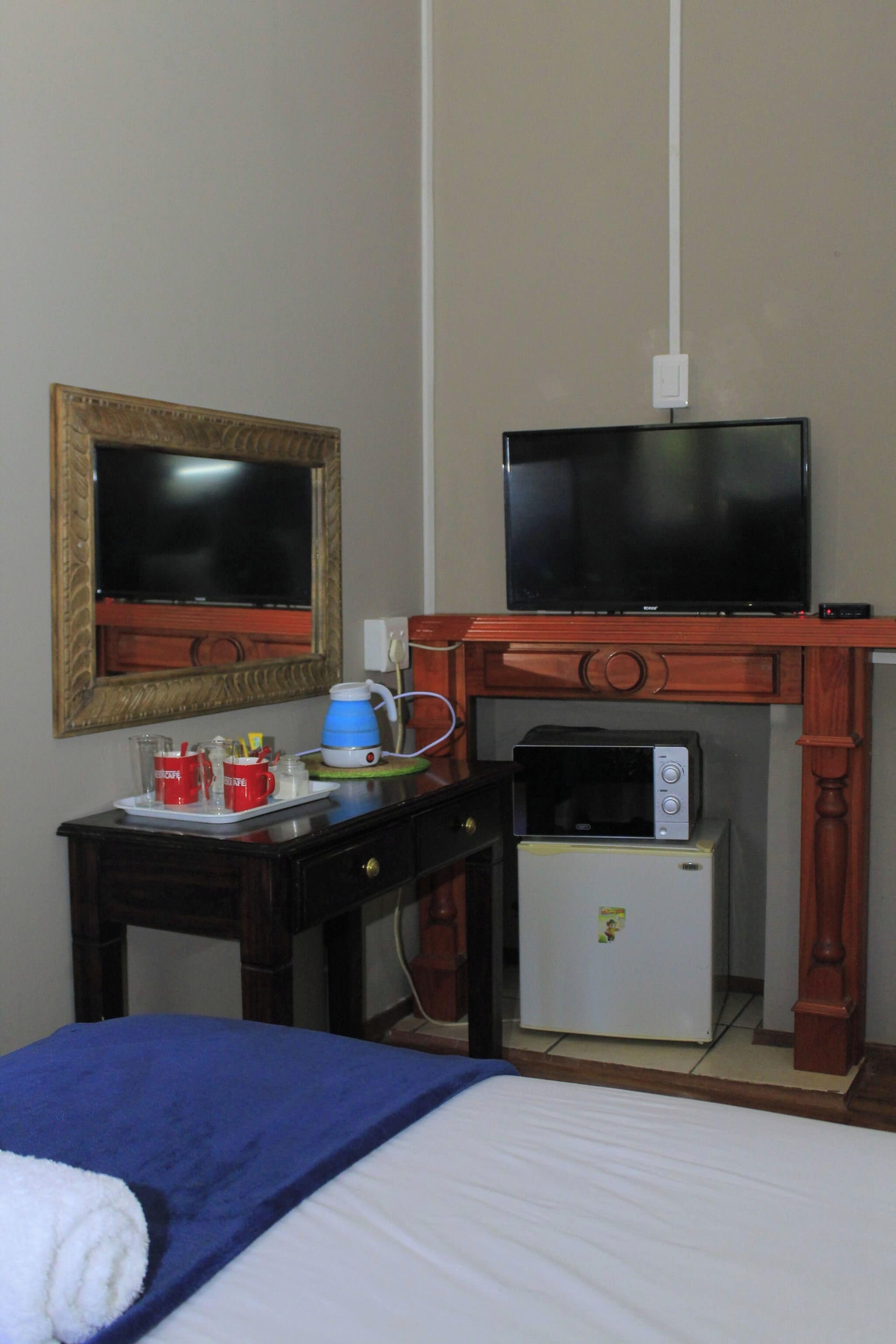 A hotel room with a bed, a television, a small refrigerator, a coffee maker, and a cup of coffee on a tray.