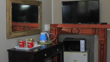 A hotel room with a bed, a television, a small refrigerator, a coffee maker, and a cup of coffee on a tray.