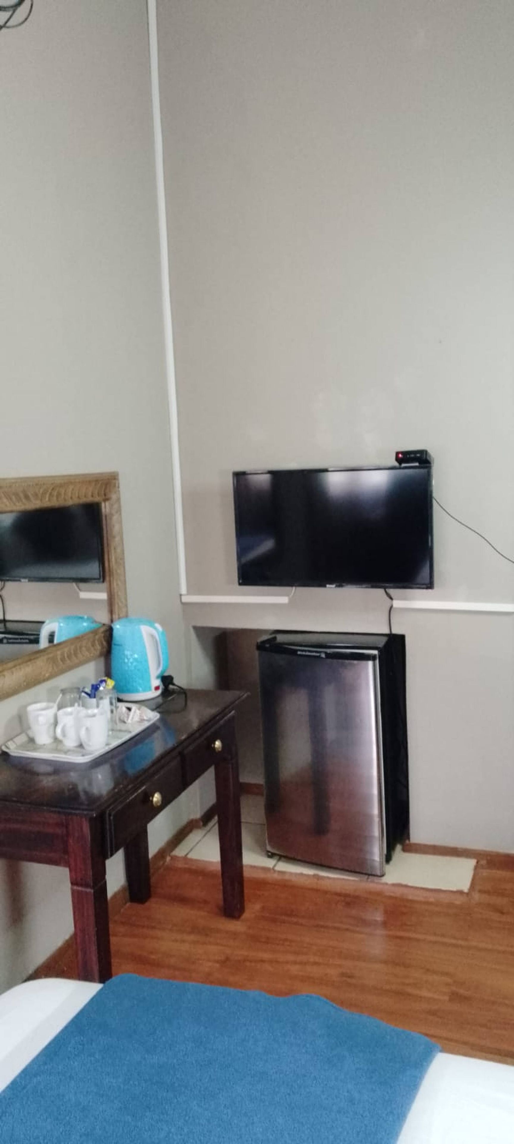 Ein Hotelzimmer mit einem Bett, einem kleinen Tisch mit Tassen und einer Fernseher, der an der Wand befestigt ist, sowie einem kompakten Kühlschrank.