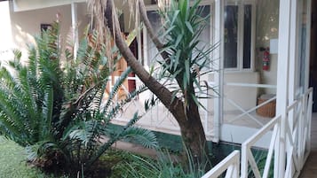 Un edificio con fachada blanca, puerta de vidrio y un pequeño jardín con diversas plantas.