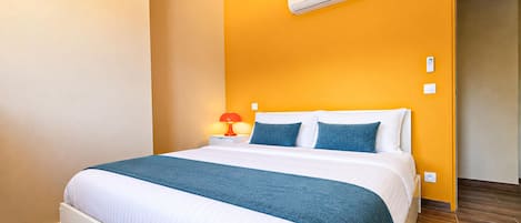 Ein Hotelzimmer mit Bett, Nachttisch, Lampe, Klimaanlage und Holzboden.