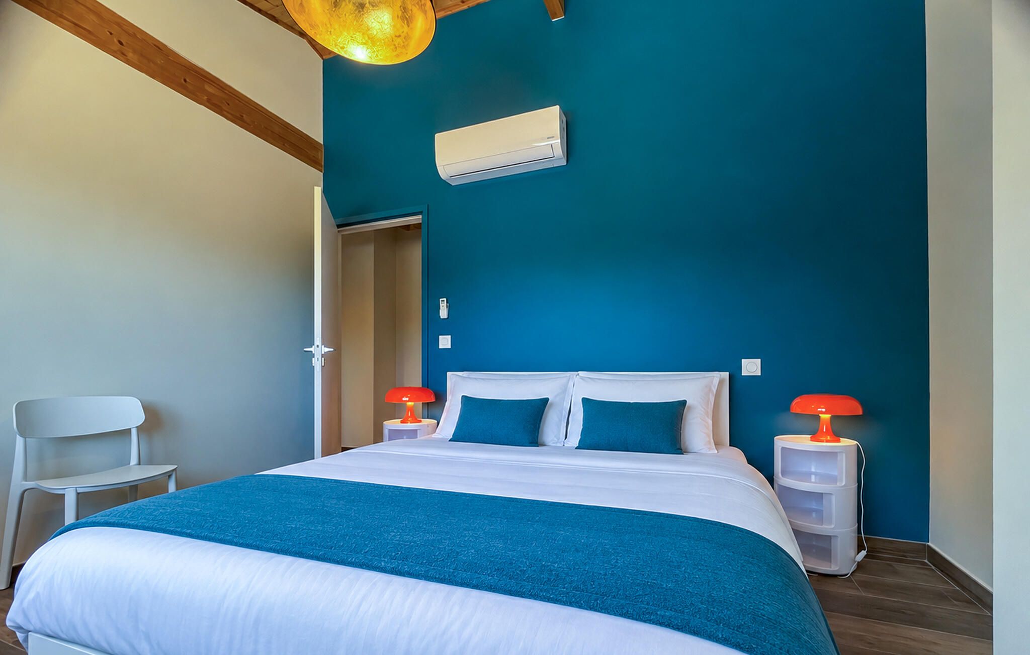 Une chambre à coucher avec un lit, deux lampes de chevet, un appareil de climatisation et une chaise blanche.