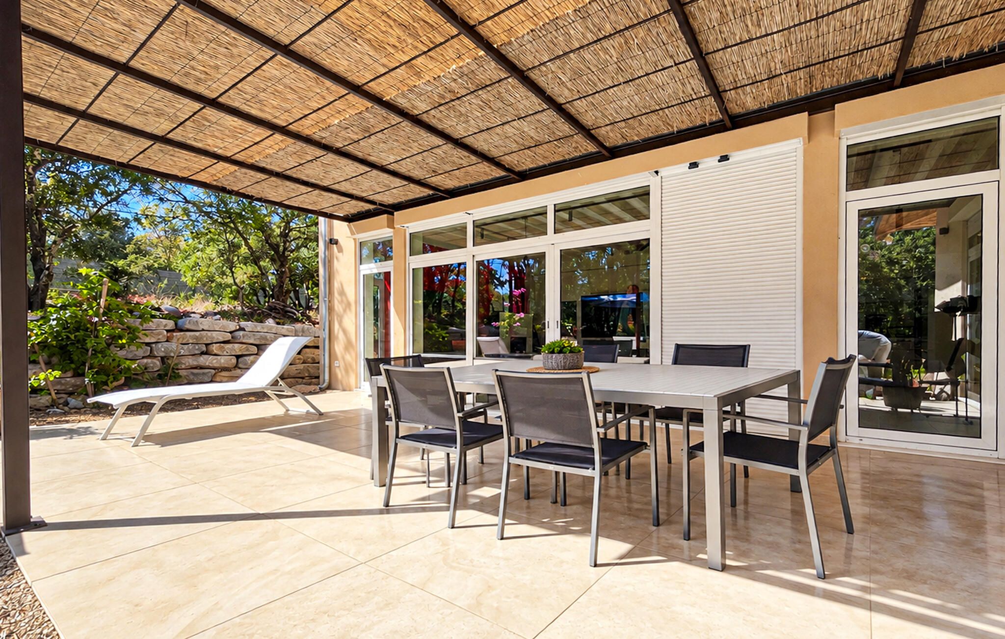 An outdoor patio with a table and chairs, a sun lounger, and a stone wall.