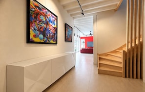 A hallway with a white console table, a staircase with wooden steps, and two large abstract paintings on the wall. - Maison piscine au calme (Méjannes-Le-Clap)