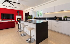A modern kitchen with a central island, white cabinetry, and a red accent wall. - Maison piscine au calme (Méjannes-Le-Clap)