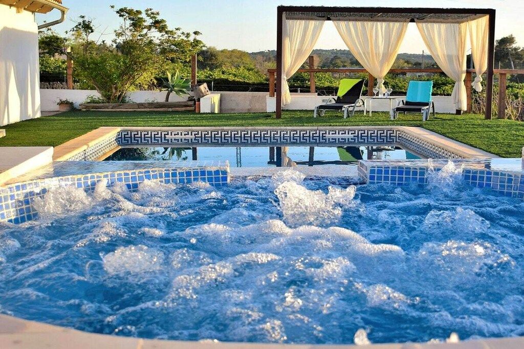 Un bain à remous dont le bord est recouvert de carreaux, entouré d’un jardin agrémenté d’une pergola et de chaises longues.