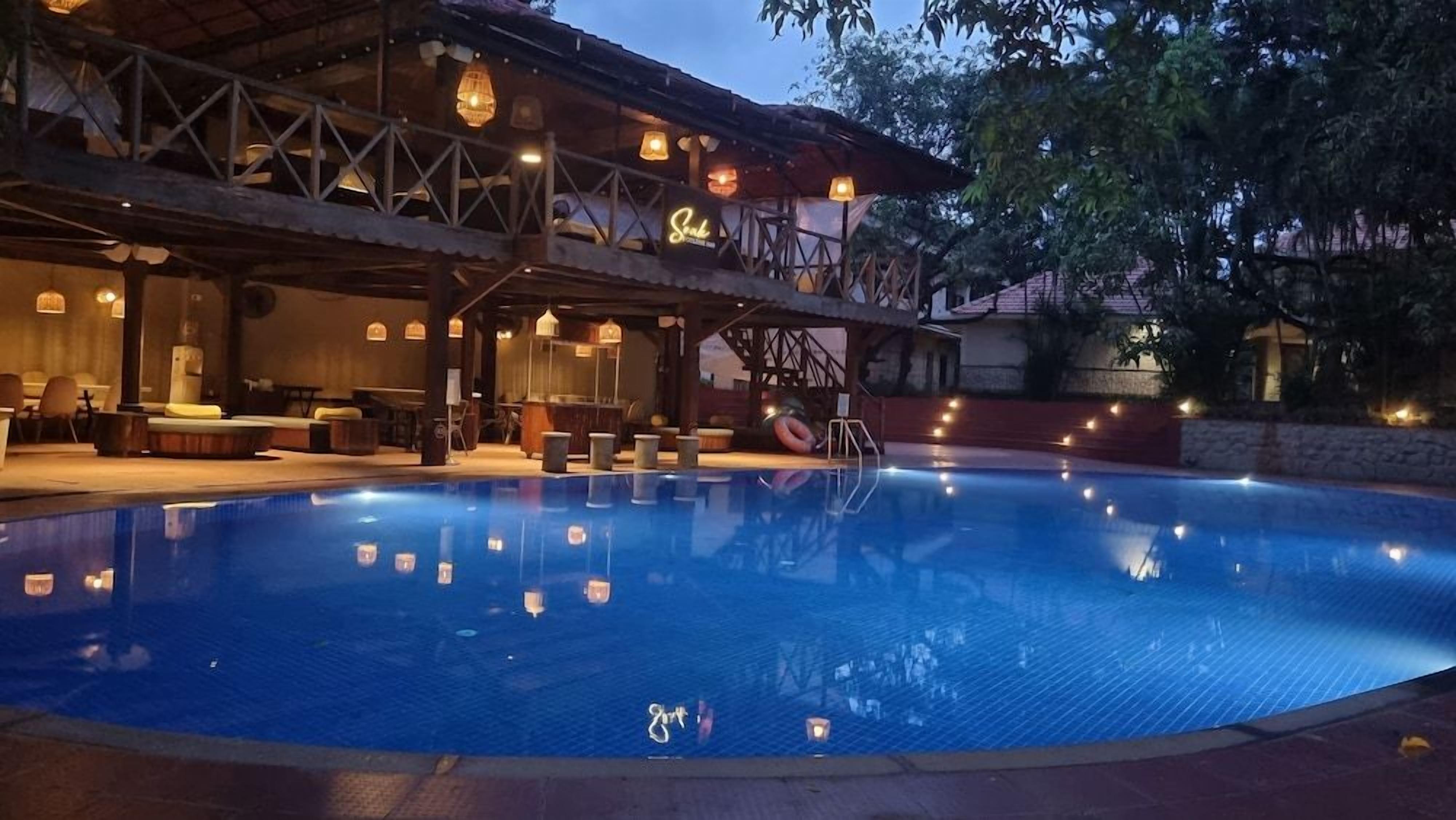A swimming pool with a covered seating area and hanging lights.