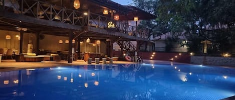 A swimming pool with a covered seating area and hanging lights.