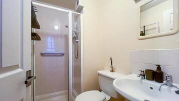 A bathroom with a glass-enclosed shower, a white toilet, and a sink with a mirror above it.