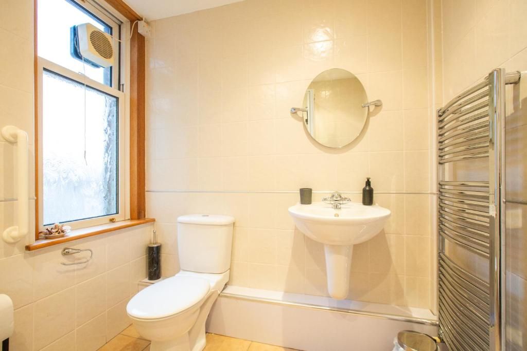 A bathroom with a toilet, sink, mirror, and a window.