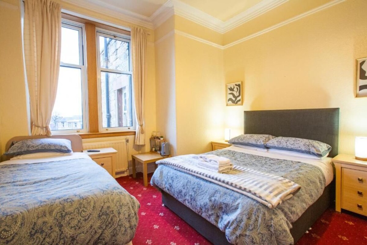 Une chambre d’hôtel avec deux lits, une fenêtre avec des rideaux, une table de chevet avec une lampe et une œuvre d’art accrochée au mur.