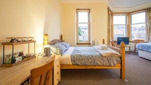 Un dormitorio con cama, escritorio con lámpara, silla, televisor y ventana con vistas.
