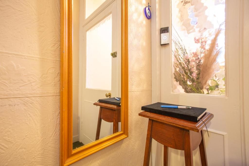 A bathroom with a large mirror, a small wooden stool, and a window with a view of flowers.