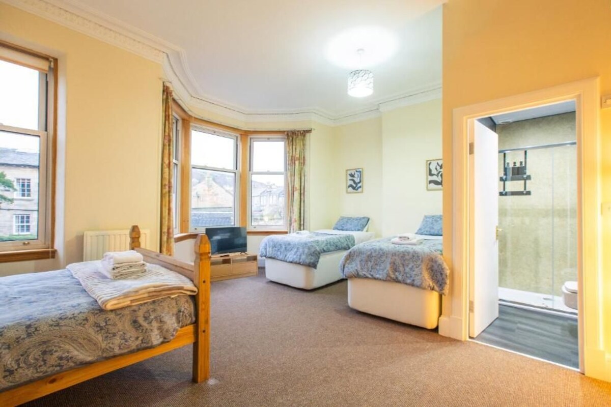 Une chambre avec un grand lit, deux petits lits, une télévision et une salle de bain visible à travers une porte en verre.