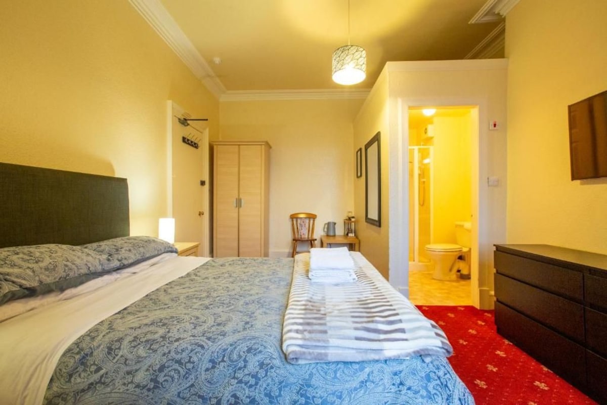 Une chambre d’hôtel avec un grand lit, une armoire, une table de chevet et une moquette rouge.