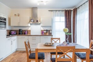 A modern kitchen with white cabinets, a wooden dining table, and a vase with flowers. - Strandresidenz Börgerende (Börgerende)