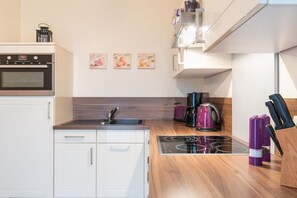 A modern kitchen with white cabinets, a built-in oven, a gas stove, and a coffee maker. - Strandresidenz Börgerende (Börgerende)