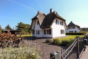 A traditional house with a steeply pitched roof, a well-maintained garden, and a paved driveway. - Holiday home with 2 bedrooms (Fuhlendorf)