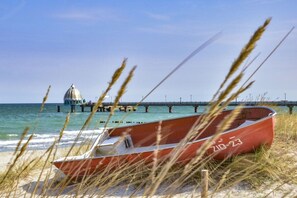 A beach with a red boat, a pier, and a building in the background. - Holiday home with 2 bedrooms (Fuhlendorf)