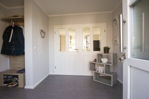A hallway with a white door, a coat rack, a small shoe storage unit, and a grey shelf with decorative items. - Holiday home with 2 bedrooms (Fuhlendorf)