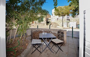 An outdoor seating area with a table and two chairs, a stone wall, and a view of a street with buildings. - Studio dans maison de village (Casalabriva)