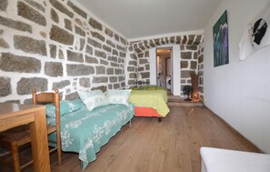 A room with a stone wall, a bed with patterned bedding, a wooden chair, and a table. - Studio dans maison de village (Casalabriva)