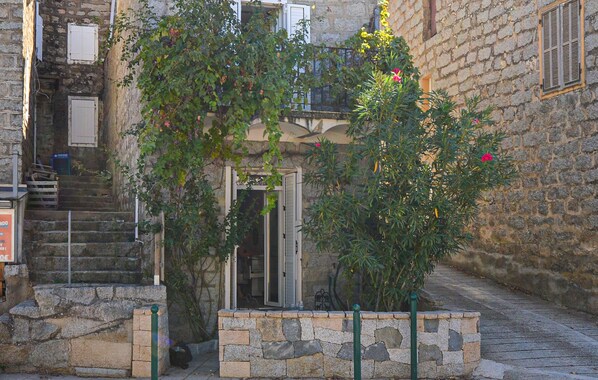 A stone building with a staircase leading to a door, surrounded by greenery and a stone wall. - Studio dans maison de village (Casalabriva)