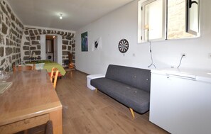 A cozy living space with a wooden dining table, a gray sofa, and a stone wall. - Studio dans maison de village (Casalabriva)