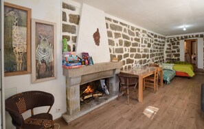 Ein gemütliches Wohnzimmer mit Steinwand, Kamin, Esstisch und einem Bett mit grüner Decke.
