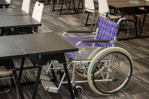 Uma cadeira de rodas com capa azul xadrez, uma mesa e cadeiras em um quarto com carpete estampado.