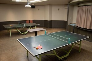 A room with two ping pong tables, one with a ball and paddle, and another with a ball and paddle.